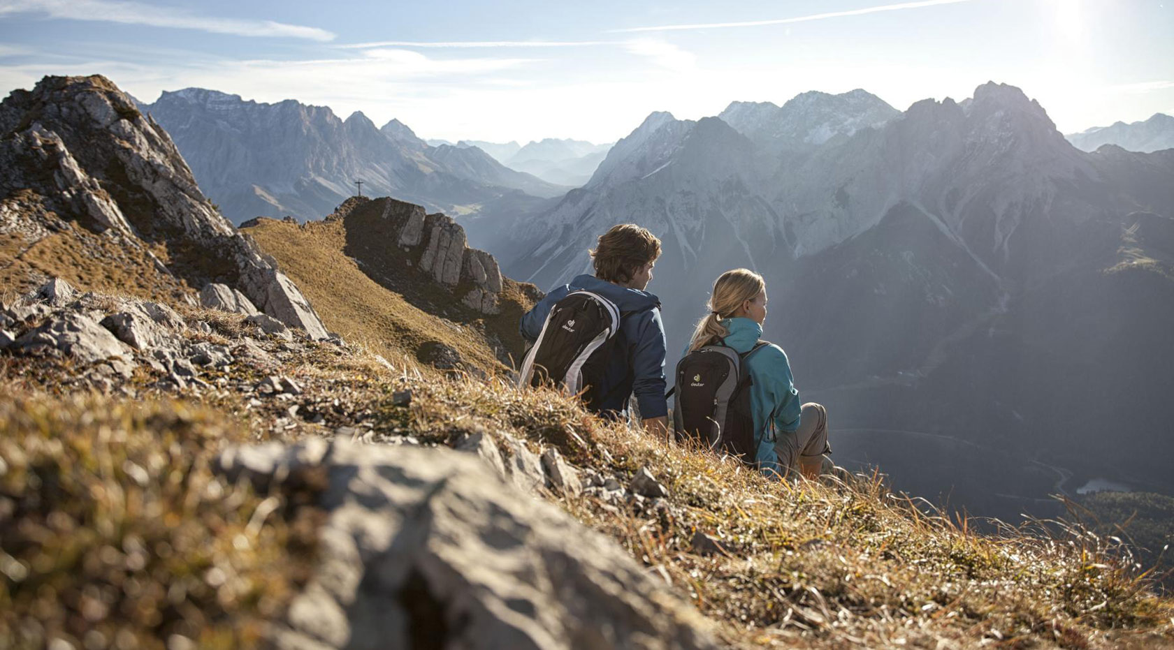 Wanderpaar sitzt auf Bergwiese mit Blick auf Alpenpanorama in der Zugspitzregion.