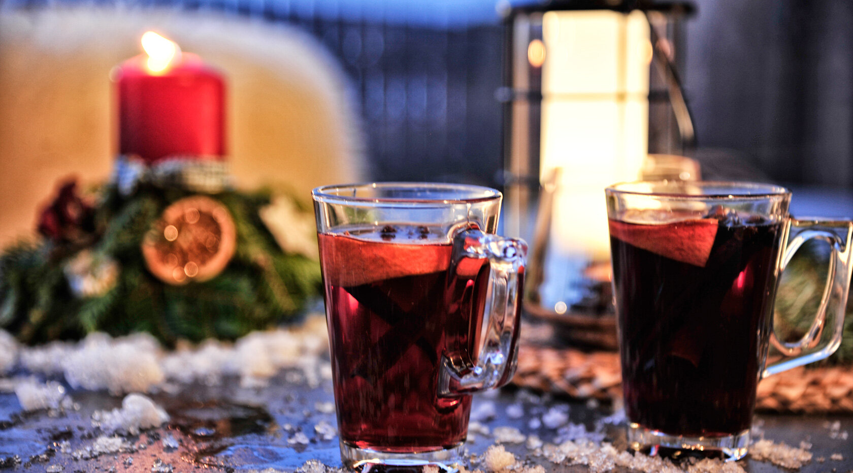 Zwei Gläser Glühwein auf verschneitem Tisch mit Kerzenlicht, Weihnachtsdeko und gemütlicher Winterabend-Stimmung.