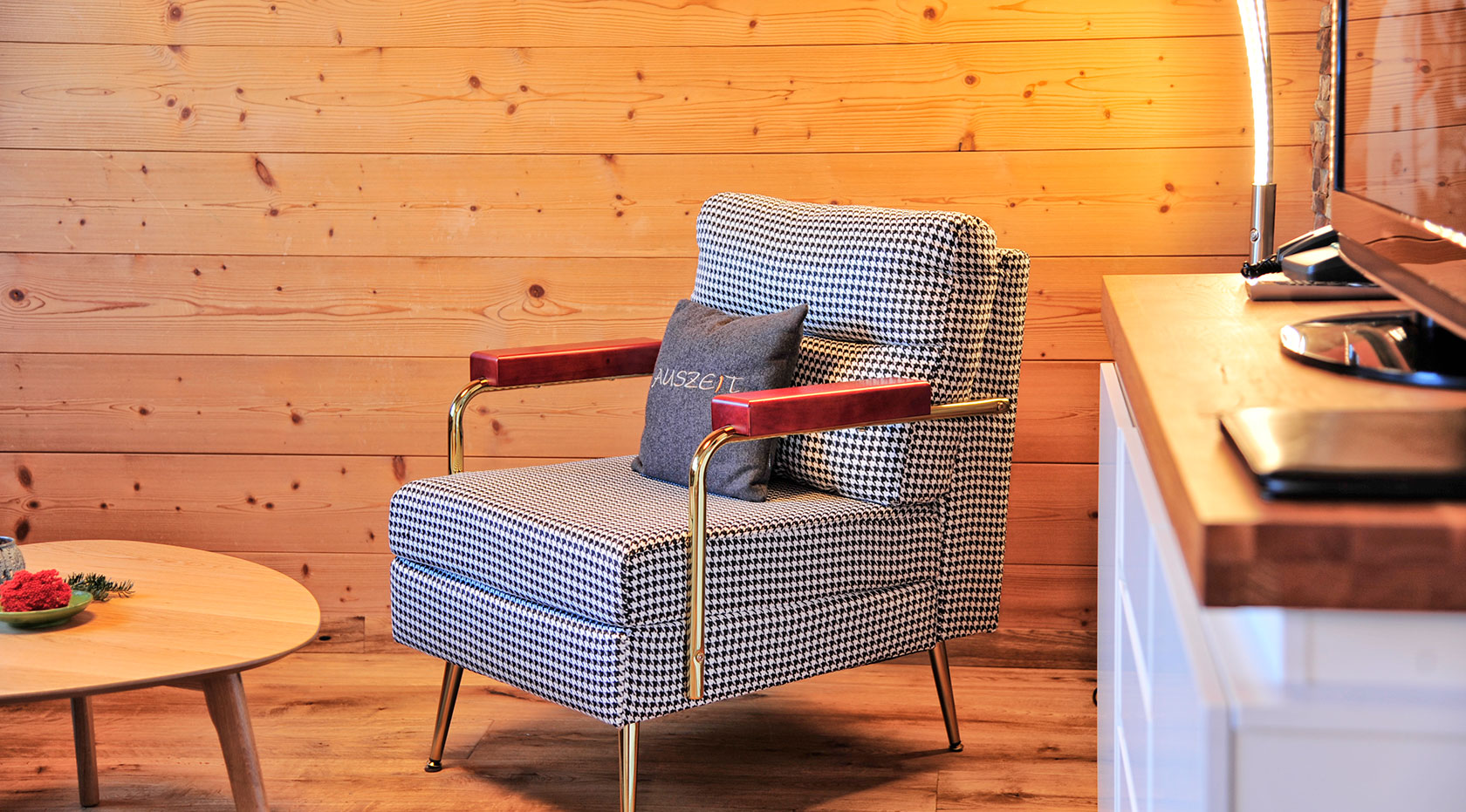 Gemütlicher Wohnbereich in einer Ferienwohnung mit Holzvertäfelung, Sessel mit Kuscheldecke und warmem Licht, Küchenzeile im Hintergrund – Ferienwohnungen Wiesenruh.